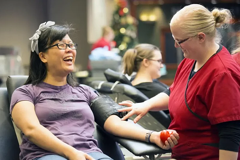 A Red Cross collection staff member prepares to take a blood donation from a donor. 