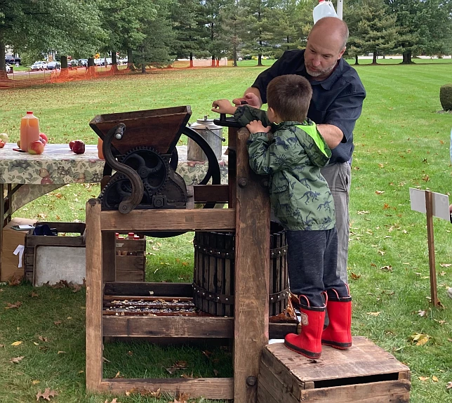 A church volunteer helps a child press apples to make cider. 