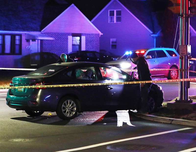 Police investigate the scene of the shooting, as two bullet exit holes are visible on the passenger's side door. 