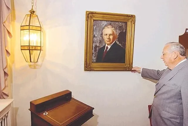 Shelly-Dinan Funeral Home owner Tim Dinan adjusts a portrait hanging on the parlor wall of Elmer Shelly, who founded the company in 1914, ahead of pla