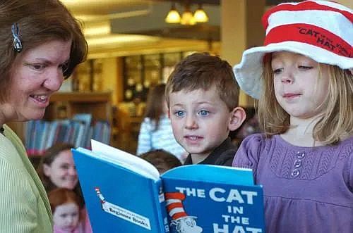 Cole Stadler, center, and Maddie Brown move in for a close look at at illustration in the Dr. Seuss book “The Cat in the Hat” as it is read to them by