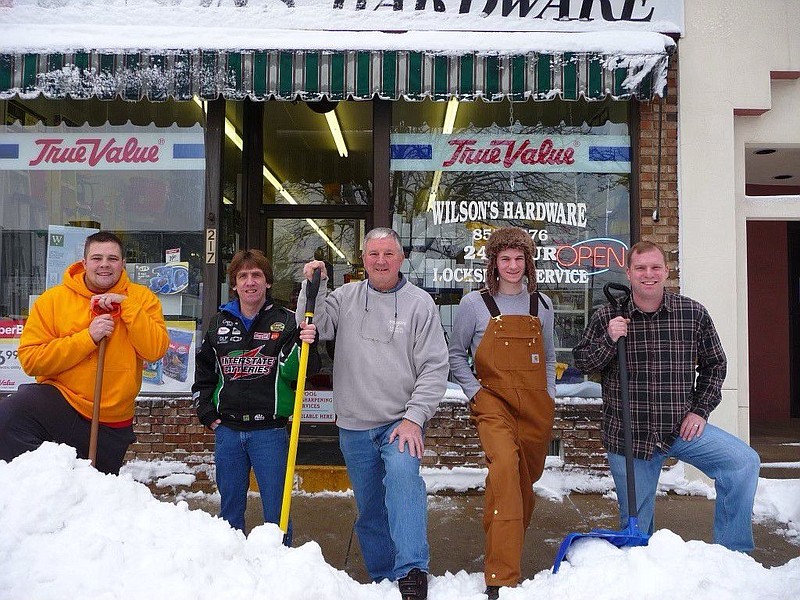 Former Wilson’s Hardware owner Joe Flyzik, who sold the business to current owners Charles and Toni Venezia, stands center in front of his former busi