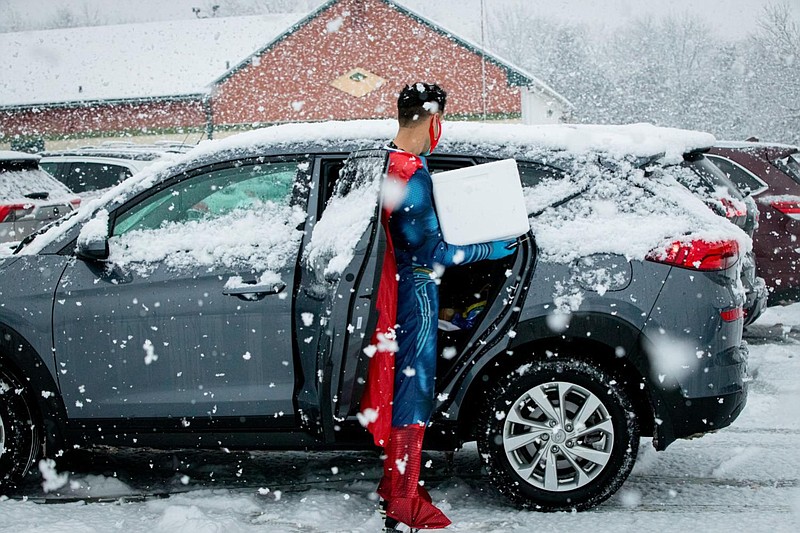 Mayank Amin, dressed as Superman, helps patients out of the car, carrying a box of doses of the COVID-19 vaccine. 