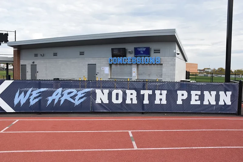 A banner reading “We are North Penn” hangs along the track near the concession stand at North Penn High School’s Crawford Stadium. 