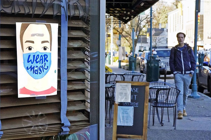 A man walks past a restaurant in Mount Lebanon, Pa., with a sign in the window that reminds people to wear a mask, Wednesday, Nov. 18, 2020. 