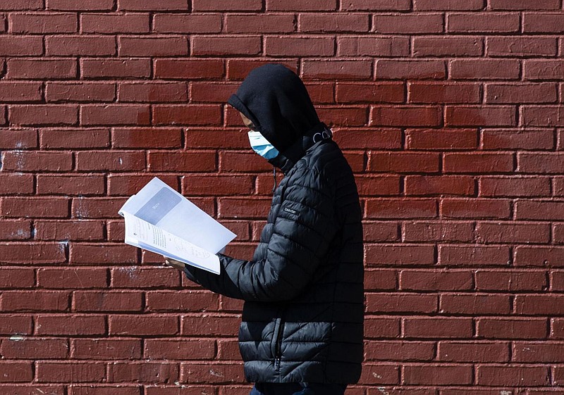 In this Thursday, March 26, 2020, photo, Terrell Bell, wearing a protective face mask, looks at a learning guide he picked up for his little sister at