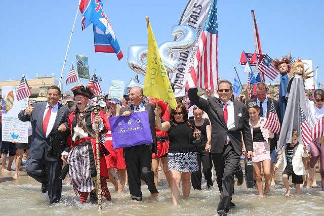 Business Persons Plunge organizer John Walton holds the American flag as he leads the march into the water.