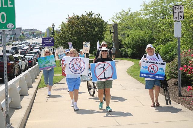 Anti-wind farm protesters walk across the Route 52 causeway bridge while holding signs denouncing the projects.