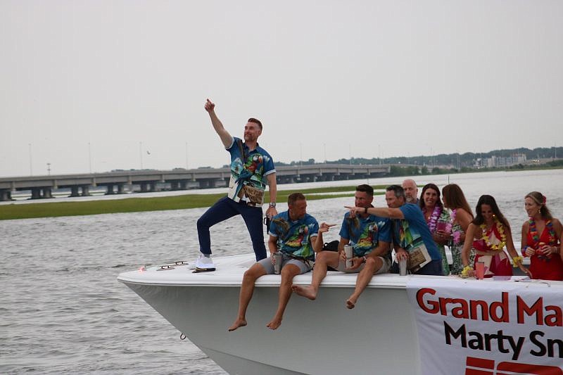 Grand Marshal Marty Smith points to spectators while standing on the bow of the boat.