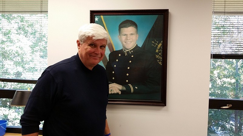 Bill Elliott stands next to a photo of his late son, Navy Ensign John Elliott.