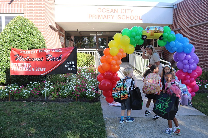 Primary School Principal Cathy Smith leads a group of students through an archway of colorful balloons decorating the front entrance.