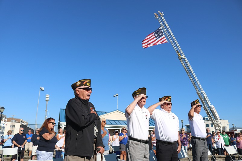 Veterans salute while a large American flag hovers over the ceremony.