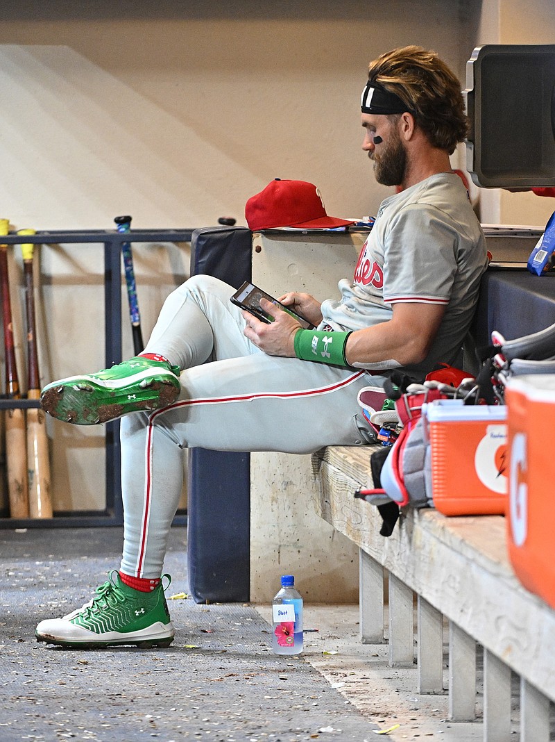 Sep 16, 2024; Milwaukee, Wisconsin, USA; Philadelphia Phillies first base Bryce Harper (3) looking over some images in the dugout in the top of the eighth inning against the Milwaukee Brewers at American Family Field. Mandatory Credit: Michael McLoone-Imagn Images