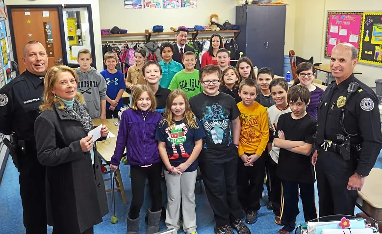 Jane Keyes, second from left, owner of the Tex Mex Connection in North Wales, stopped by a fifth grade classroom at North Wales Elementary School to present a $2,500 donation to the school’s DARE program in January 2015. At left is North Wales police patrol and DARE officer Terry Hammerstone, and at right is then-police chief Alex Levy. In the background are then-principal Joseph T. Covone III, standing next to fifth grade teacher Melissa Deets and students in Deets’ class. (Credit: MediaNewsGroup)