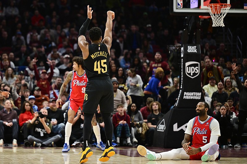 Dec 21, 2024; Cleveland, Ohio, USA; Cleveland Cavaliers guard Donovan Mitchell (45) shoots a three point basket as Philadelphia 76ers center Andre Drummond (5) sits on the court and watches during the first half at Rocket Mortgage FieldHouse. Mandatory Credit: Ken Blaze-Imagn Images