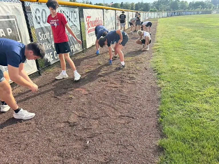 North Penn Knights baseball players pick weeds from the warning track at their ballfield adjacent to North Penn High School in Aug. 2024. (Credit: Facebook/North Penn Knights Baseball)