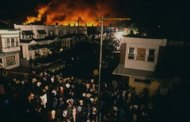 West Philadelphia residents gather during the fire from the bomb dropped on the MOVE home on Osage Ave. on May 13, 1985. (Credit: Wikipedia)