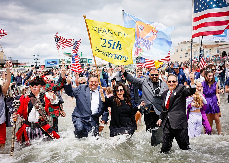 John Walton and Stacy Demcher, both dressed in black outfits, lead the charge into the ocean. (Photo courtesy of Kerri J Photography and Ocean City)