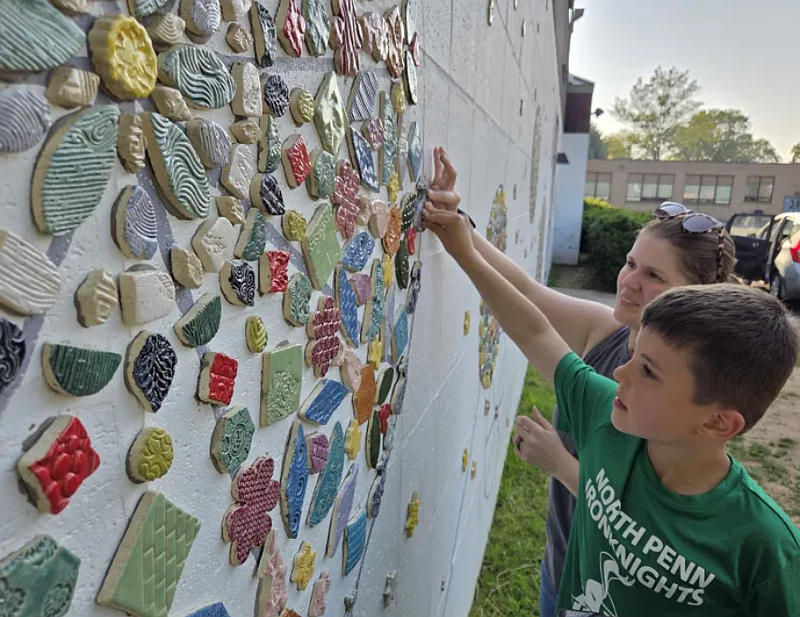 Kindergartner Max Andrews and artist Laura Skidmore hold a tile as it’s added to a mosaic mural on the wall of North Wales Elementary School on Wednesday, June 4, 2025.