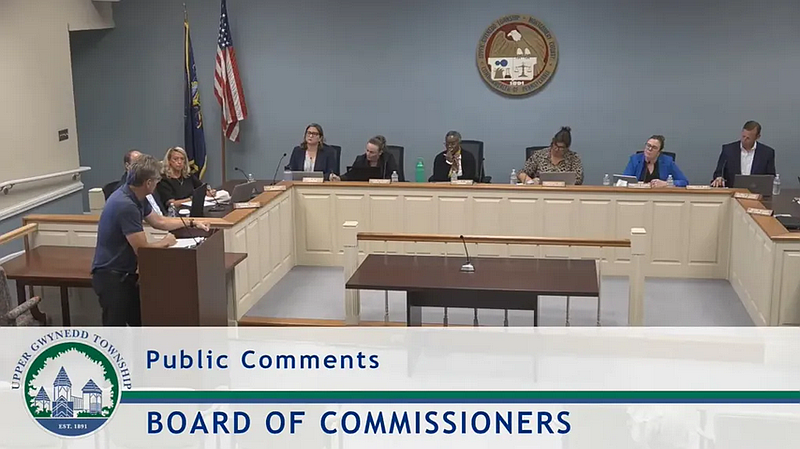 Upper Gwynedd resident Carl Smith, at podium, speaks to the township’s commissioners and officials during public comments in their Sept. 16, 2025 meeting. From left to right seated are township engineer Nick Cross, commissioners Liz McNaney and Denise Hull, solicitor Lauren Gallagher, commissioner Katherine Carter, township Manager Sandra Brookley Zadell, and commissioners Rebecca Moodie and Greg Moll. (Screenshot of meeting video)