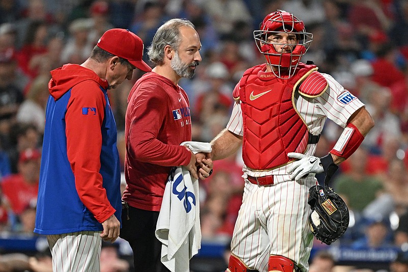 Sep 23, 2025; Philadelphia, Pennsylvania, USA; Philadelphia Phillies trainer Joe Rauch works on the hand of catcher J.T. Realmuto (10) after being injured during the ninth inning against the Miami Marlins at Citizens Bank Park. Mandatory Credit: Eric Hartline-Imagn Images