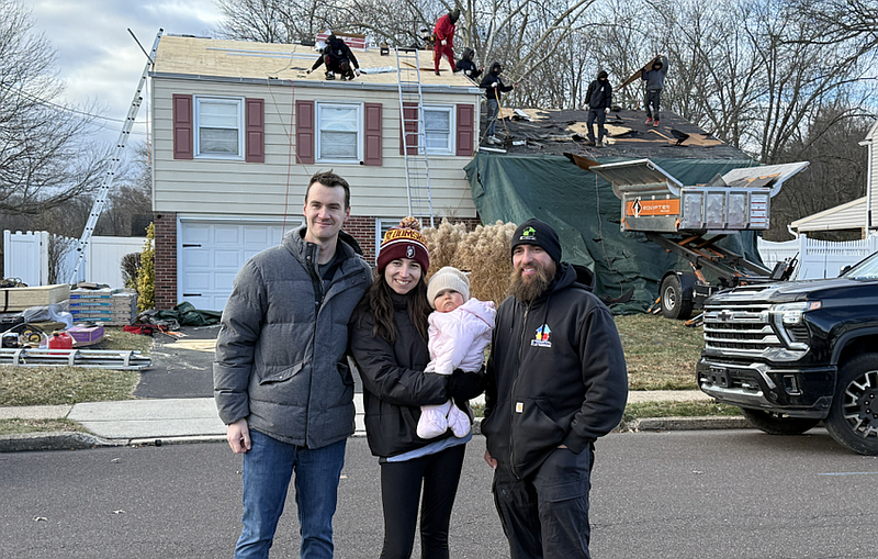Connor, Brianna and Sienna Miller (left) pose for a picture with Dan Kingkiner of Essential Exteriors (right) as the company installs the family’s new roof. (Photo by Laura Moyer)