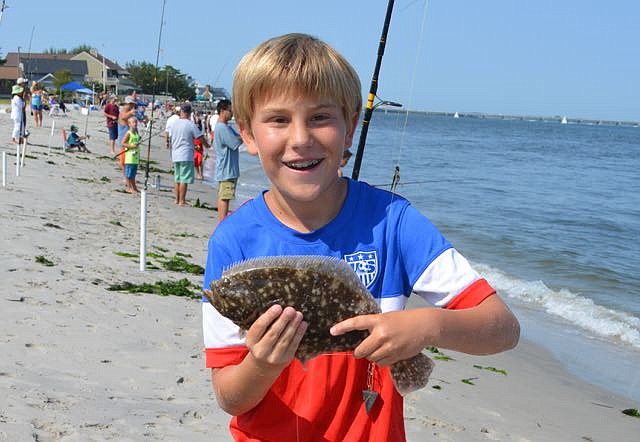 This happy youngster holds up the summer flounder he caught at last year’s tournament. Not a keeper because of its size, the fish was returned to the water.  