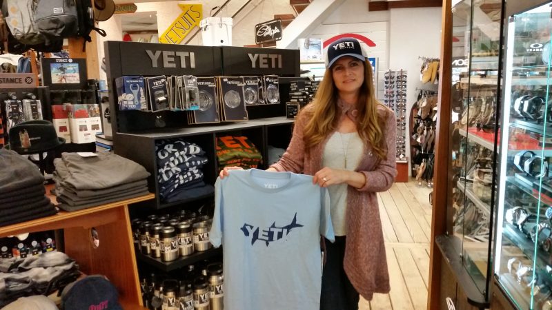 Kim DeMarco, a surf shop salesperson, models some Yeti caps and T-shirts.