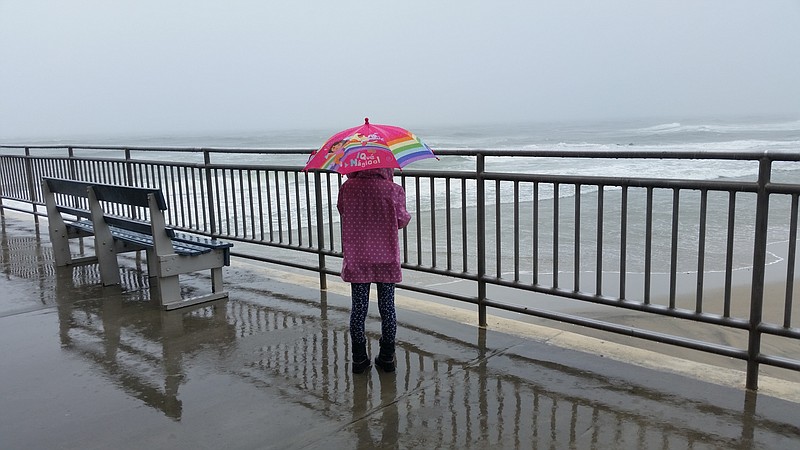 Protected by an umbrella, 7-year-old Sarah Smith, of Ocean City, peered out at the big waves on a soggy day.