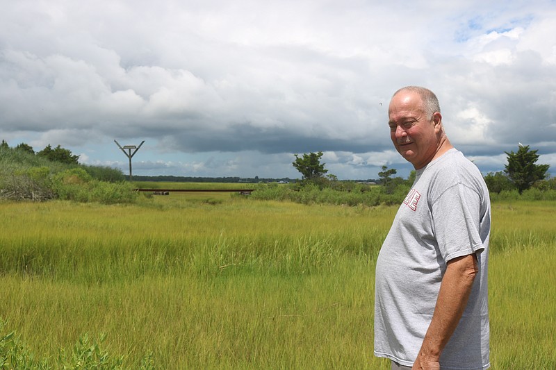 In a photo from August 2018, Ocean Aire condo owner Steve Sinibaldi points to a gap underneath an abandoned railroad track that he blames for flooding that spills out of the marshlands behind the complex.