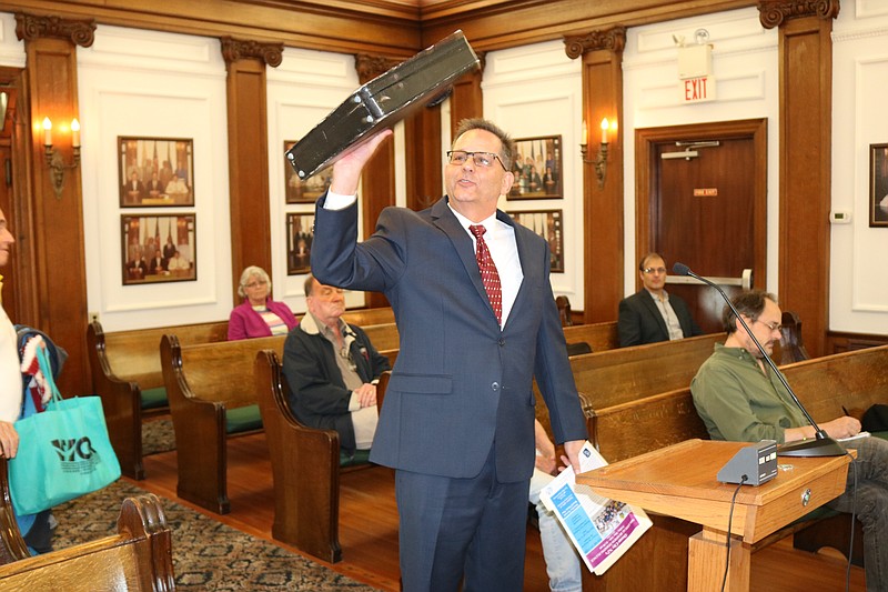 During remarks to City Council in 2019, John Walton shows off the old briefcase he always carries with him into the surf during the plunge. 