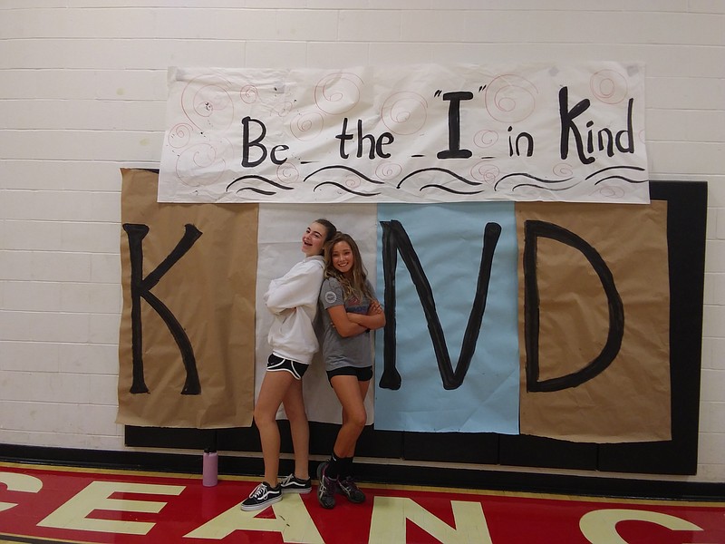 Freshmen Grace Oves, and Taylor Pontari pose next to the Be Kind poster.