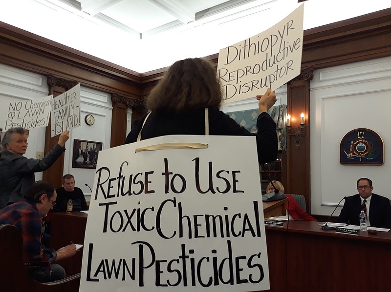 Environmental advocate Donna Moore, with back to the camera, holds up signs warning of the dangers of chemical pesticides.