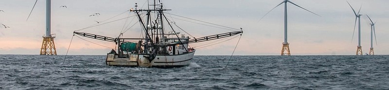 A fishing boat works near wind turbines. (Photo Credit: RODA)