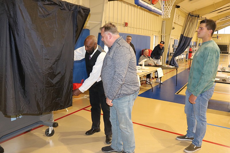 Polling worker Keith B. Parrish holds the curtain for voter Paul Stryker as he enters the booth. Stryker's son, Paul Jr., waits his turn to vote.