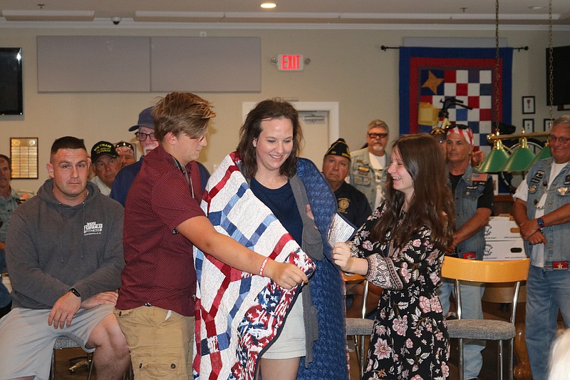 Airman First Class Glenda Williams receives a Quilt of Valor placed on her by her children, Joshua and Alcie, while her husband, Marine Staff Sgt. James Williams, looks on. 