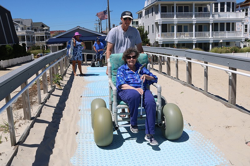 Jeff Daisher pushes his mother-in-law, Patricia Rossbauer, both of West Grove, Pa., down to the 34th Street beach along a mobility mat in August 2022.