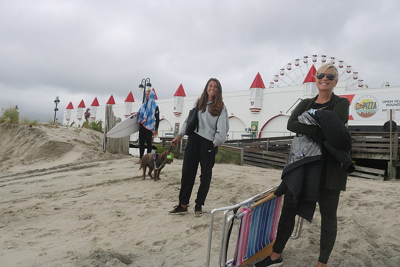 Friends Jess Kohles, left, and Cristen Ferguson, both of Philadelphia, watch their children surf while standing on the storm-eroded beach.