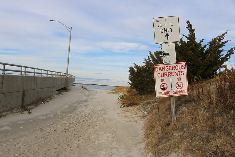 A "Dangerous Currents" sign on the beach pathway next to the bridge warns people not to swim or wade in the inlet.