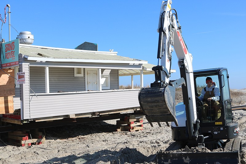 Workers dig soil out from under the building and level the ground.