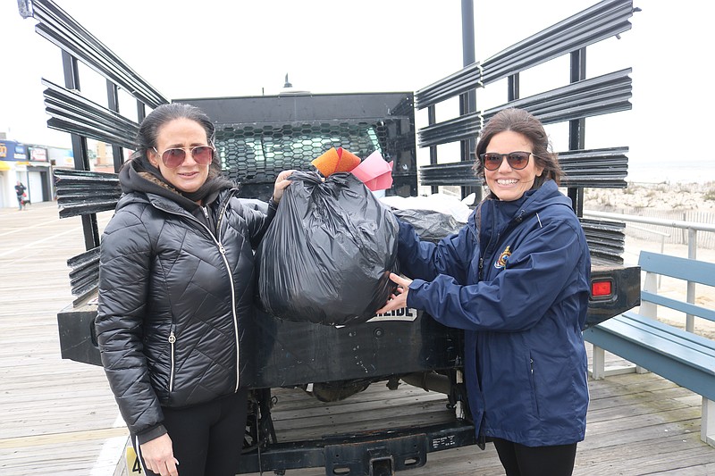 Public Works employees Kelliann Jones, left, and Victoria Puga, scoop a bag of trash into the back of the city truck.