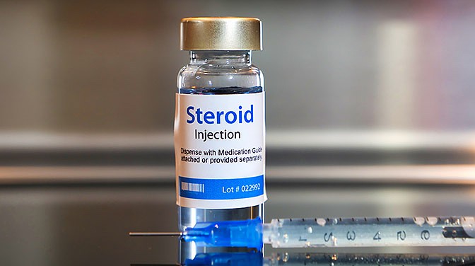 Vial of Steroid injection with a syringe on black table and stainless steel background.