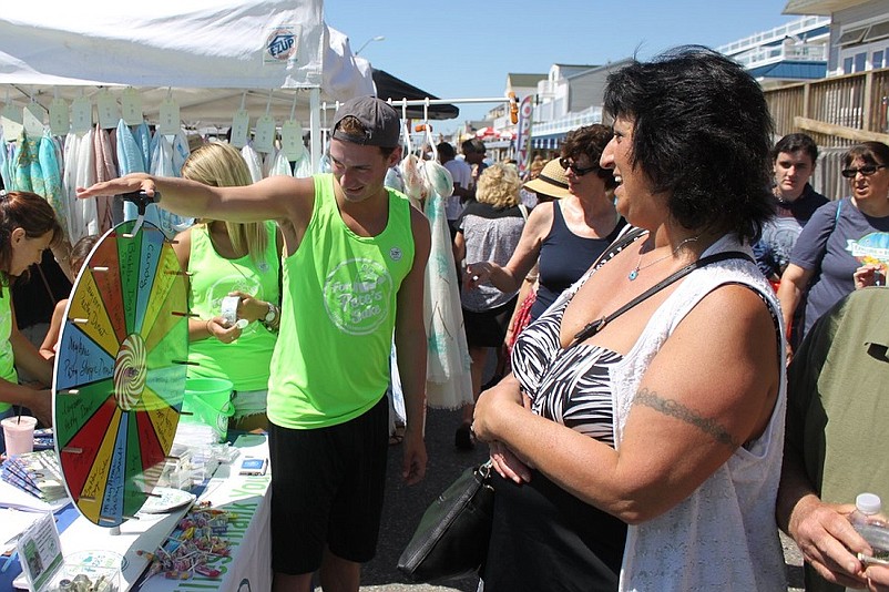  In addition to hundreds of merchandise vendors, representatives from numerous non-profit organizations manned booths along Sea Isle City’s Promenade during 2016 Skimmer Festival. Shown spinning a free gift wheel for Joanne Schork, of Broomall, PA (at right), is Albert Sica, of Bristol, PA, an intern at For Pete’s Sake, a charity that provides respite vacations for adult cancer patients. 