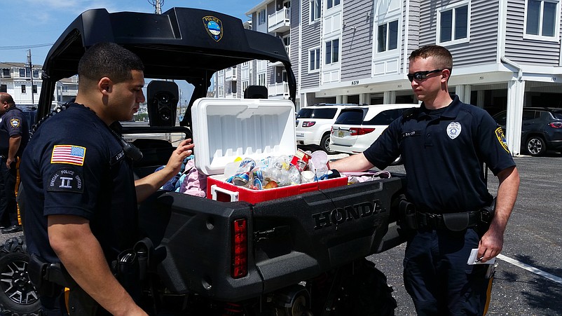 Summer police officers George Eskander, left, and Jeffrey Snyder look at a confiscated beach cooler containing beer cans and bottles.