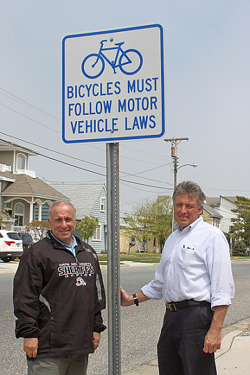 New signs have recently been installed around Sea Isle City to remind bicyclists that they must follow the same rules-of-the-road as motor vehicles. Shown with one of the new signs are Sea Isle City Mayor Leonard Desiderio (at left) and Business Administrator George Savastano.