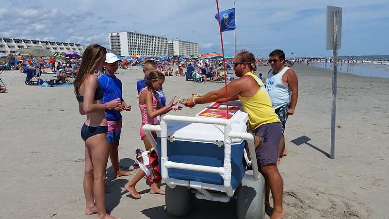 Greg Wilson, a "Fudgy Wudgy" ice cream salesman, in yellow shirt, hands out some frozen treats to beachgoers.