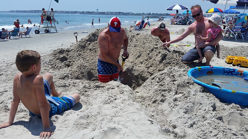 Ron Withelder, of Garnet Valley, Pa., digs on a hole on the beach while his 8-year-old son, Ray, watches, along with Chris Greenfield and his daughter, Natalie.