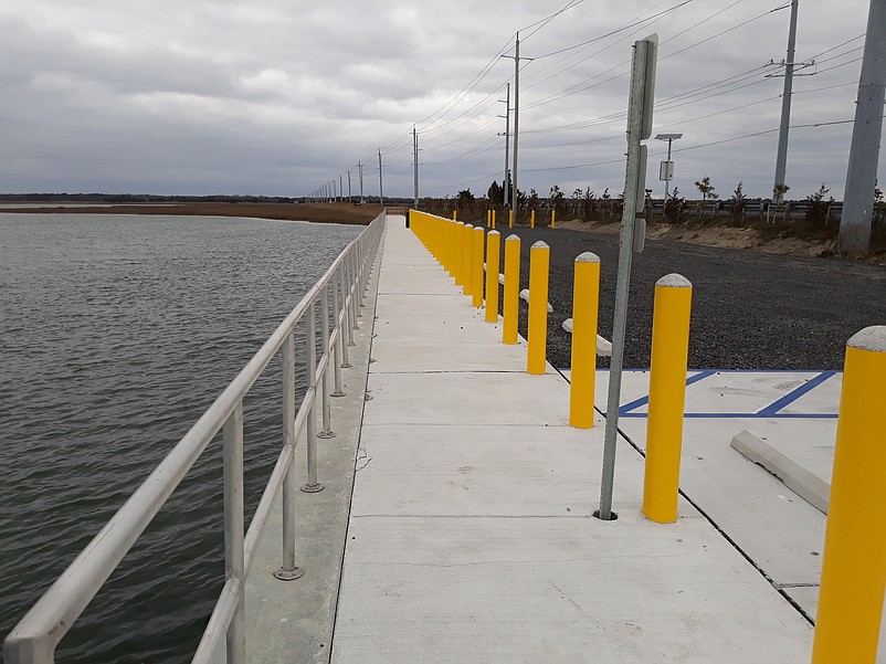 A long concrete walkway protected by a metal railing provides plenty of space for anglers and crabbers.