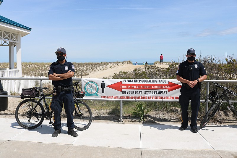 Police officers Muhammad Ali, left, and Kenzee Delgado wear face masks while standing in front of a banner on the Promenade that reminds people to practice social distancing.