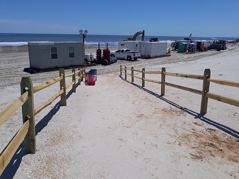 Construction equipment and trailers crowd the beach at the end of one pathway.